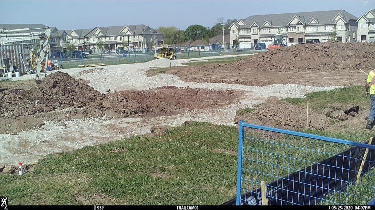 Land being zoned for construction. There is a fence in the foreground and some buildings in the background. 