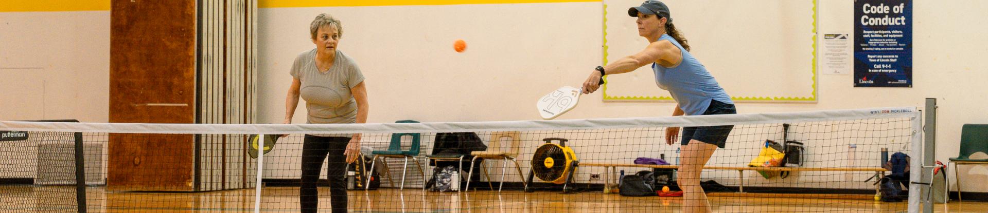 Two women playing pickleball in a gym