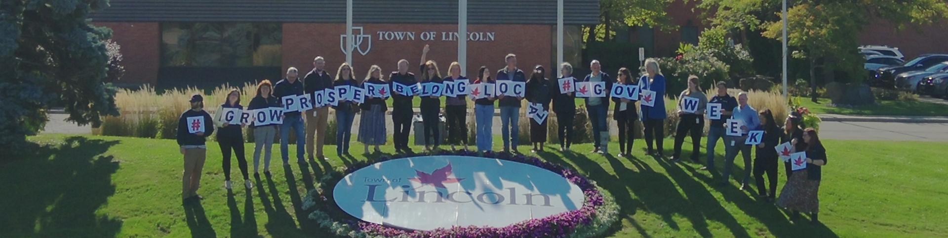 Staff carrying letter cards standing around Town of Lincoln flower bed