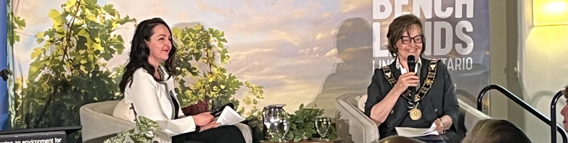 Two women sitting in front of blue sky backdrop