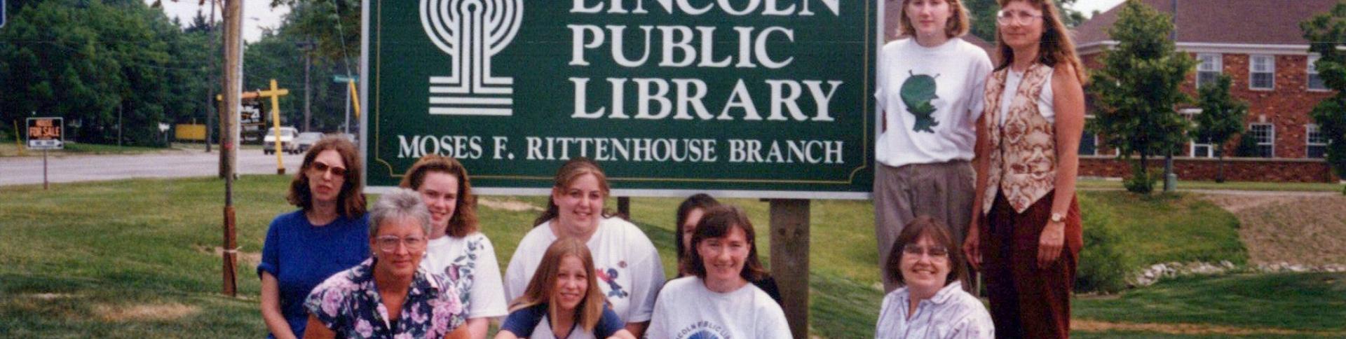 Several people gathered around old green and white Lincoln Public Library sign