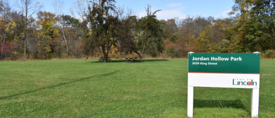 Park sign with open field and trees in background