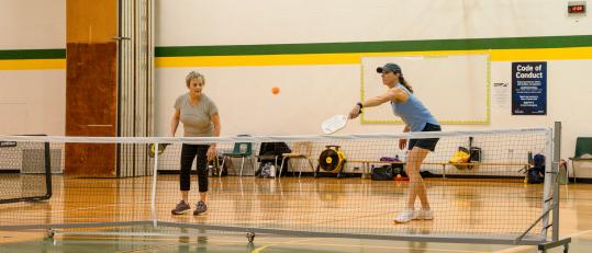 Two women playing pickleball in a gym