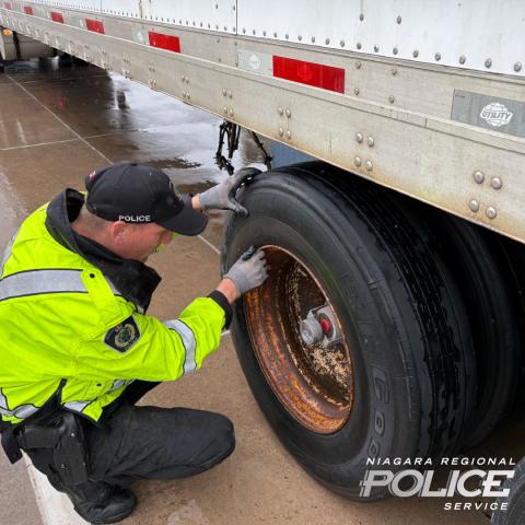 Police officer inspecting tire of transport truck.