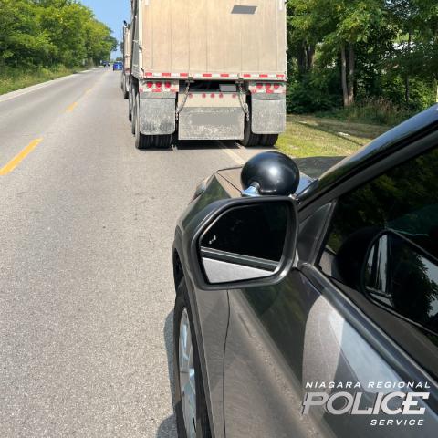Police vehicle parked behind transport truck on a road.