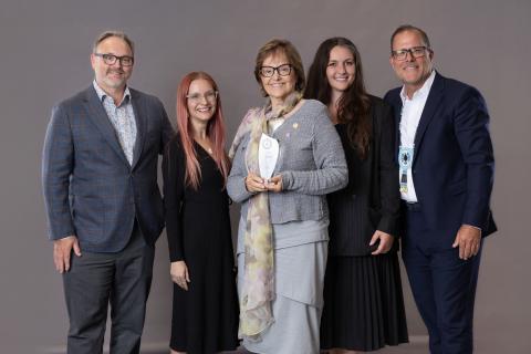 Five people in a row with centre lady holding glass award
